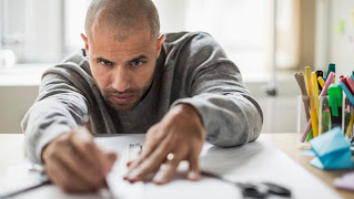 a man working with ruler and pen on a table with a large sheet of white paper and some cups of colourful pens