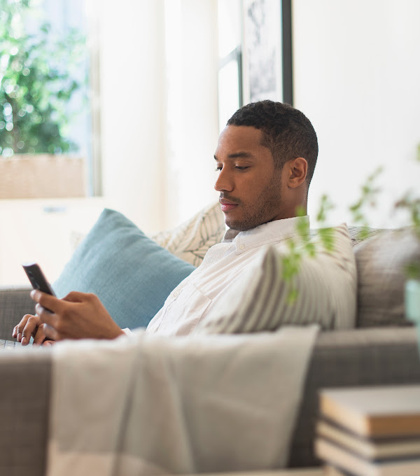 Man sitting on couch with a laptop in his lap and a mobile phone in his hand