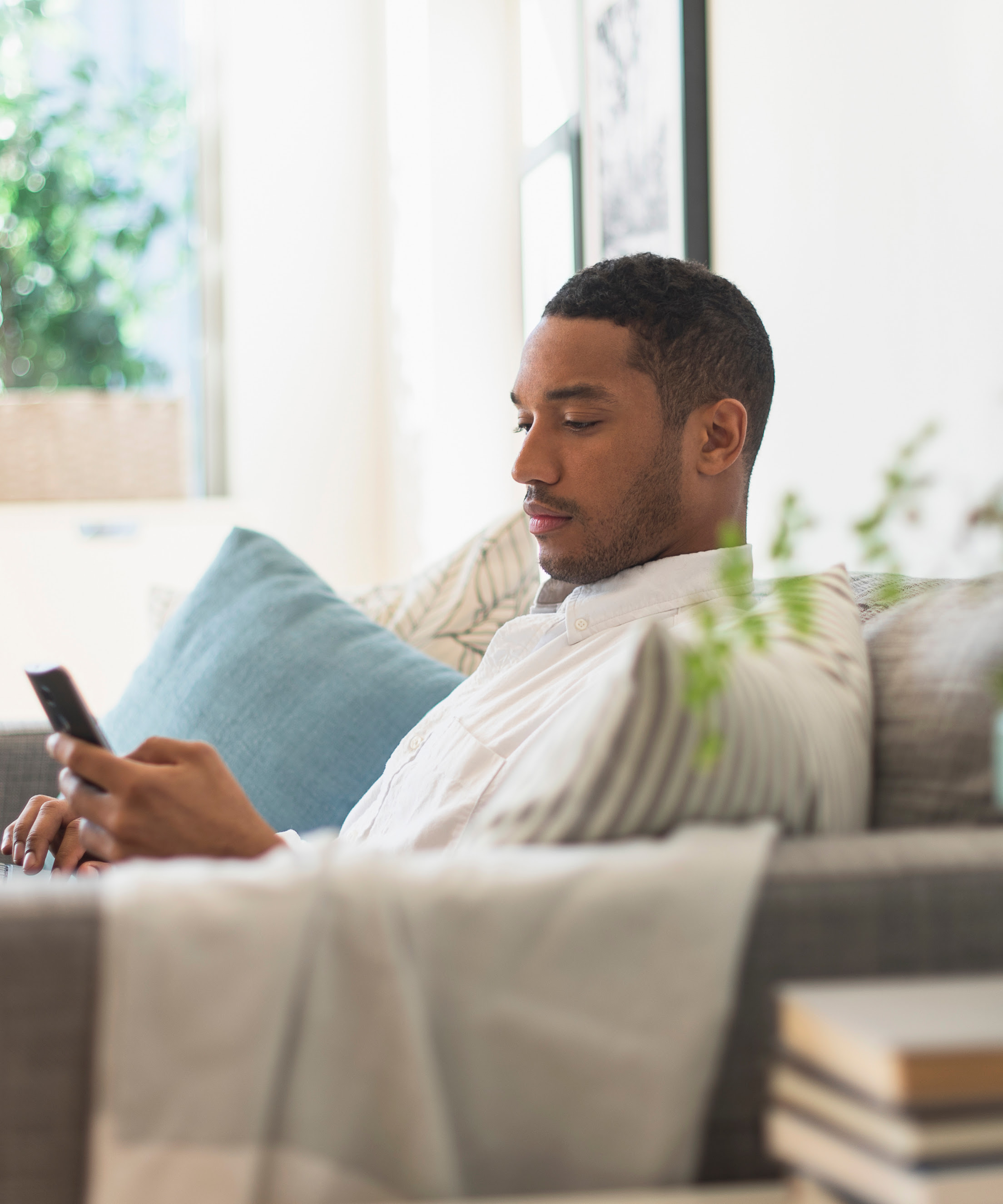 Man sitting on couch with a laptop in his lap and a mobile phone in his hand