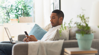 Man sitting on couch with a laptop in his lap and a mobile phone in his hand