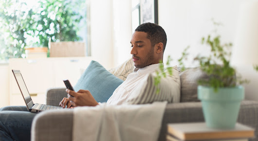 Man sitting on couch with a laptop in his lap and a mobile phone in his hand