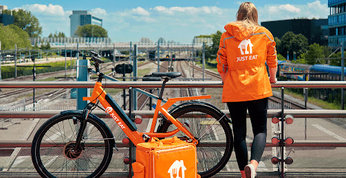 Lieferantin von Just Eat Takeaway.com, die neben ihrem Fahrrad auf einer Brücke steht