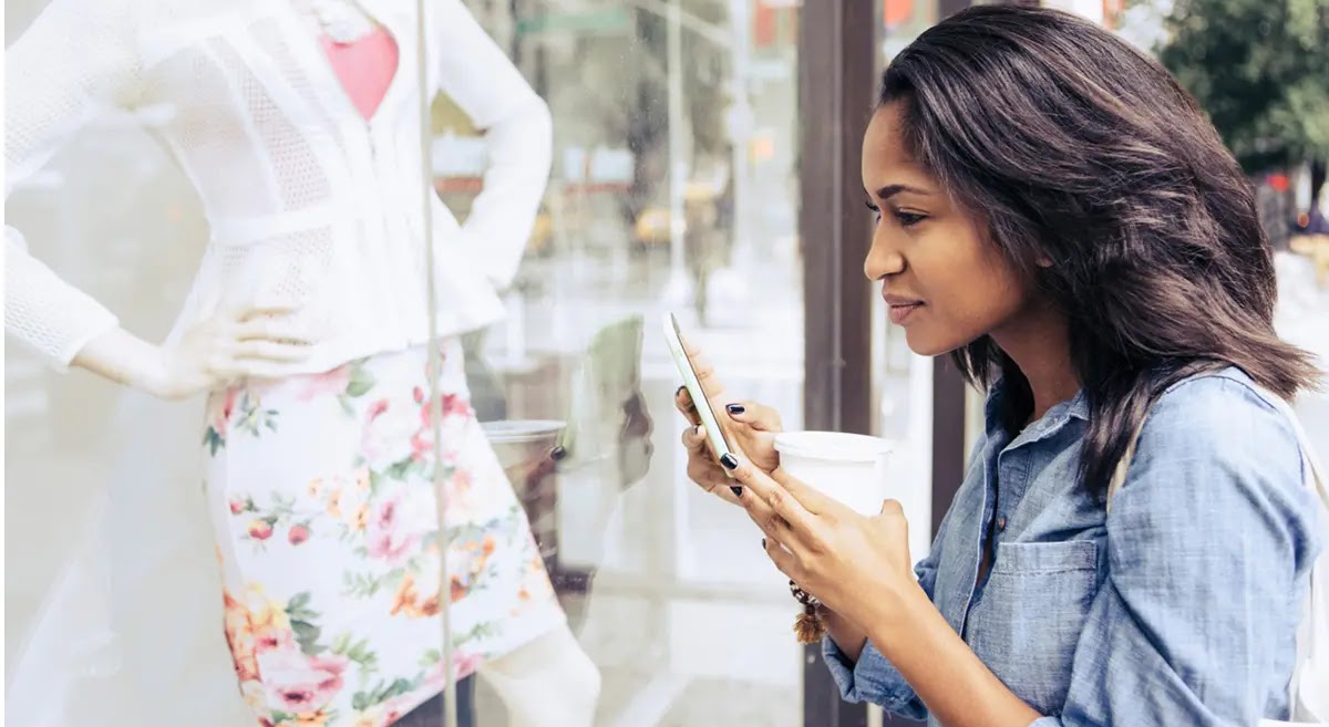 A young woman looking inside a store through the glass panel while holding her phone