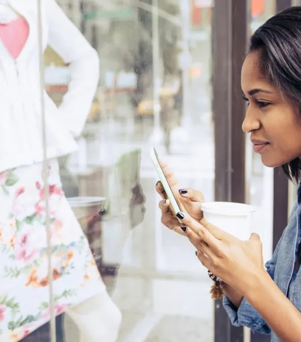 A young woman looking inside a store through the glass panel while holding her phone