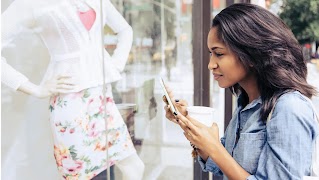 A young woman looking inside a store through the glass panel while holding her phone