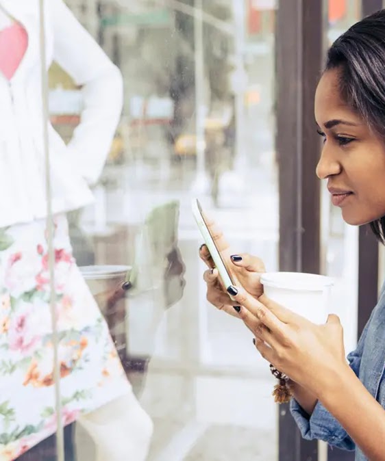 A young woman looking inside a store through the glass panel while holding her phone