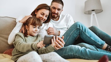 Vater, Mutter und Tochter, die mit dem Smartphone eine Sendung auf discovery+ ansehen