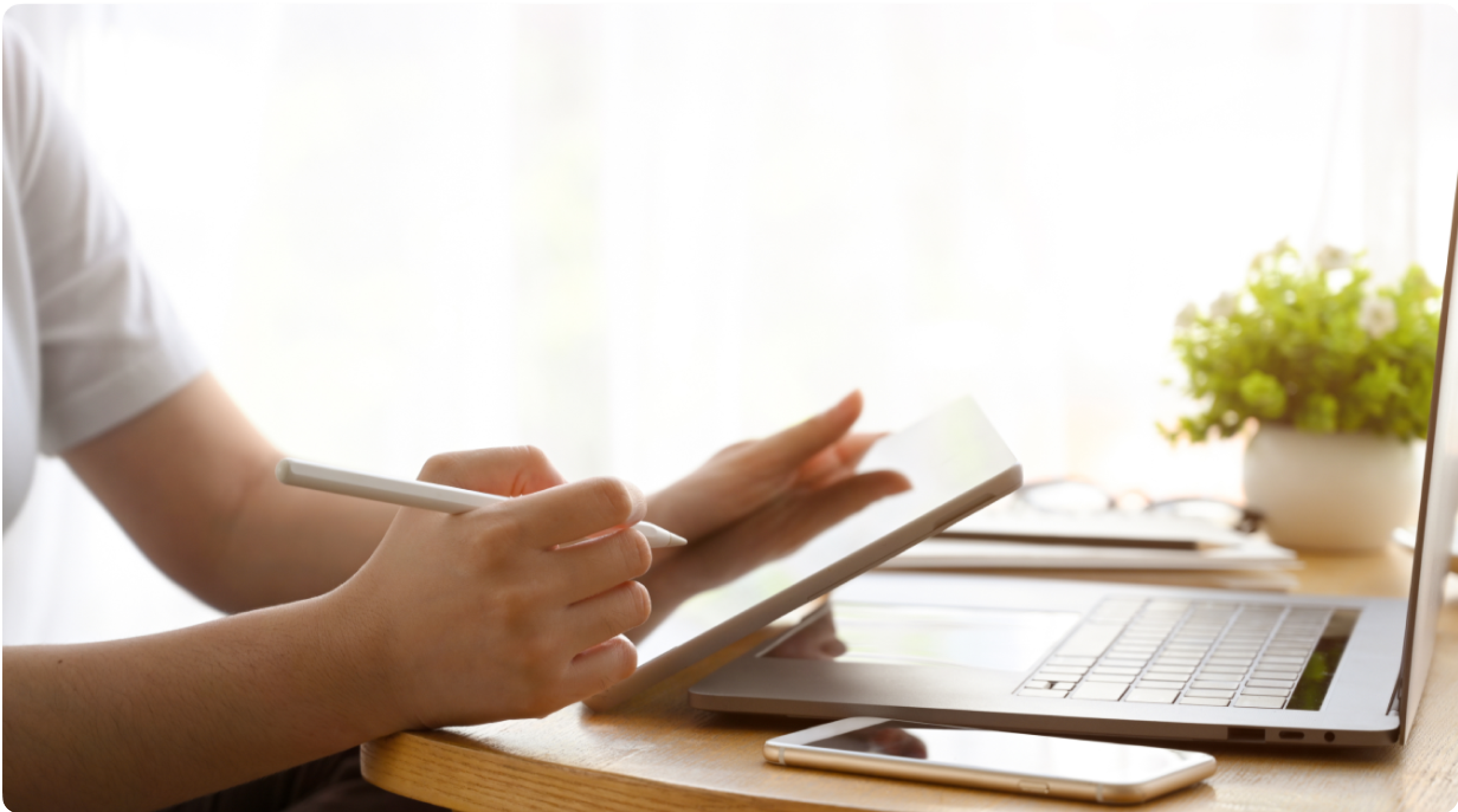 A business owner sits at home working from a tablet. An open laptop and smartphone on the table is also in front of them.