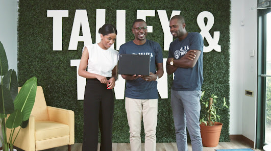 Three Talley & Twine employees standing together in front of the Talley & Twine sign in the office