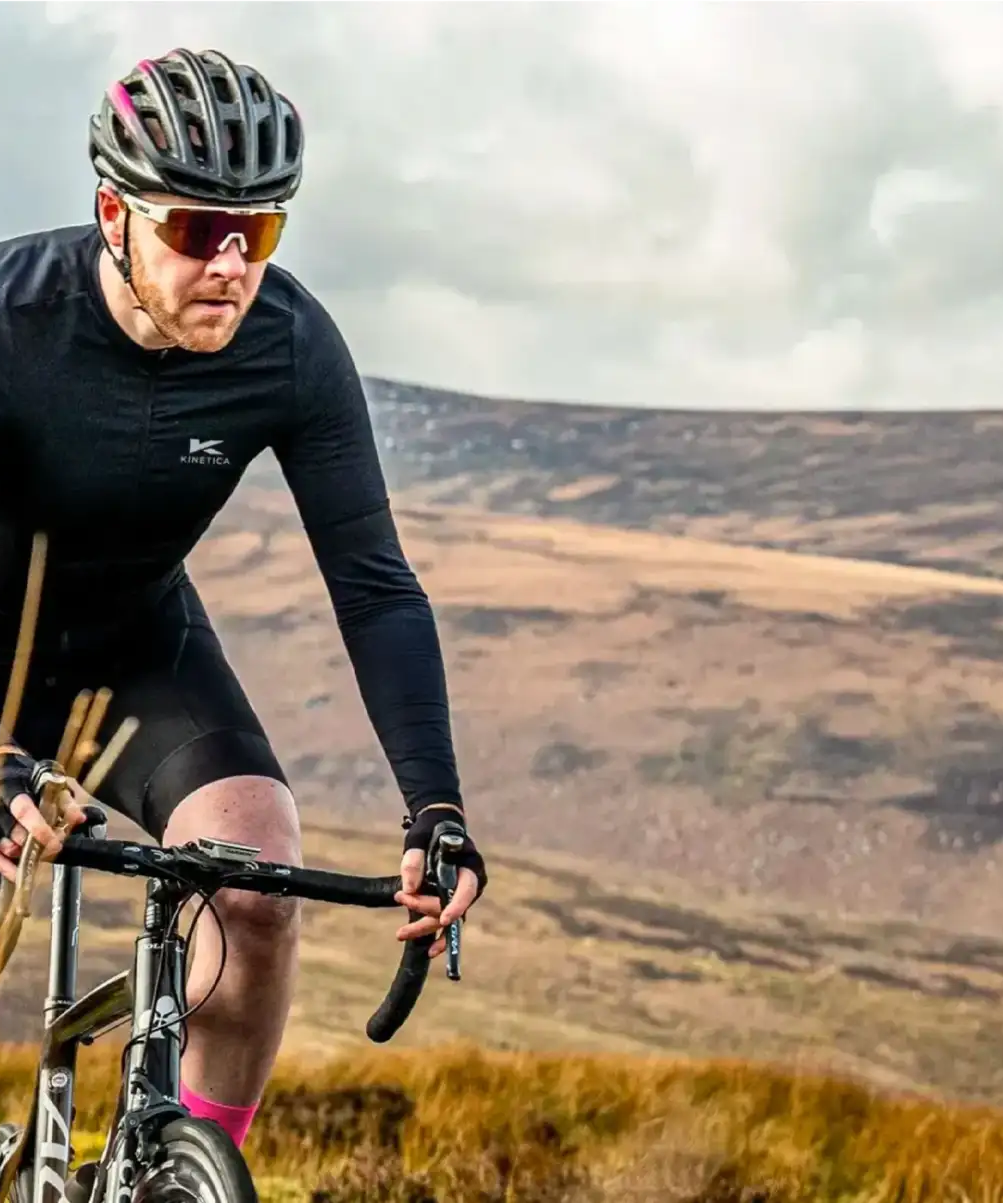 A cyclist wearing all black rides a mountain bike through the countryside.