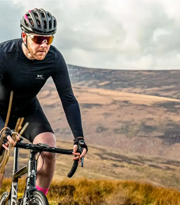 A cyclist wearing all black rides a mountain bike through the countryside.