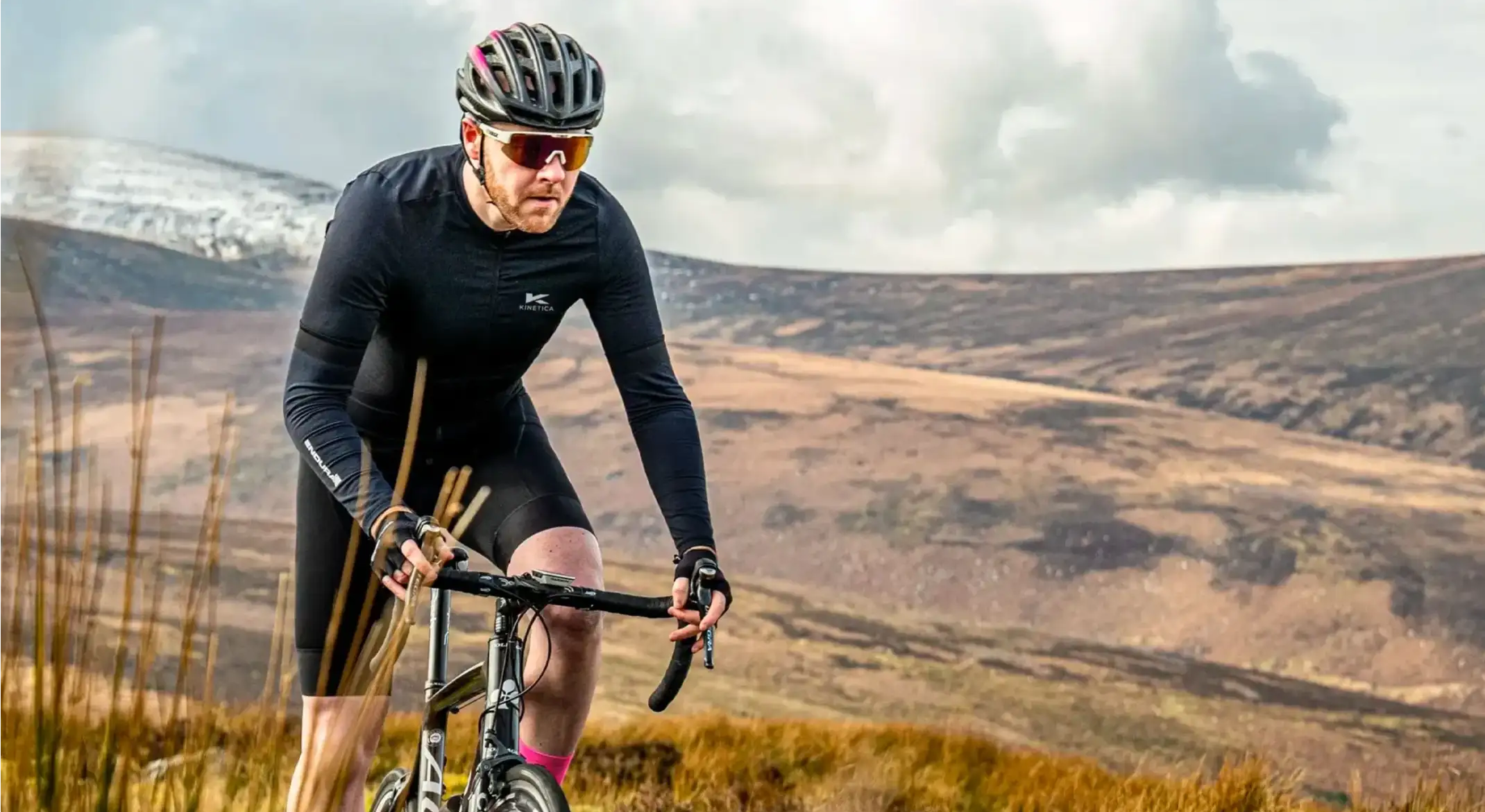 A cyclist wearing all black rides a mountain bike through the countryside.