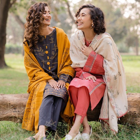 Two women sitting on a horizontal tree trunk