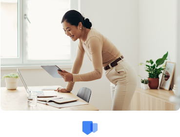 A woman leaning over her desk looking over her accolades and rewards on her tablet.