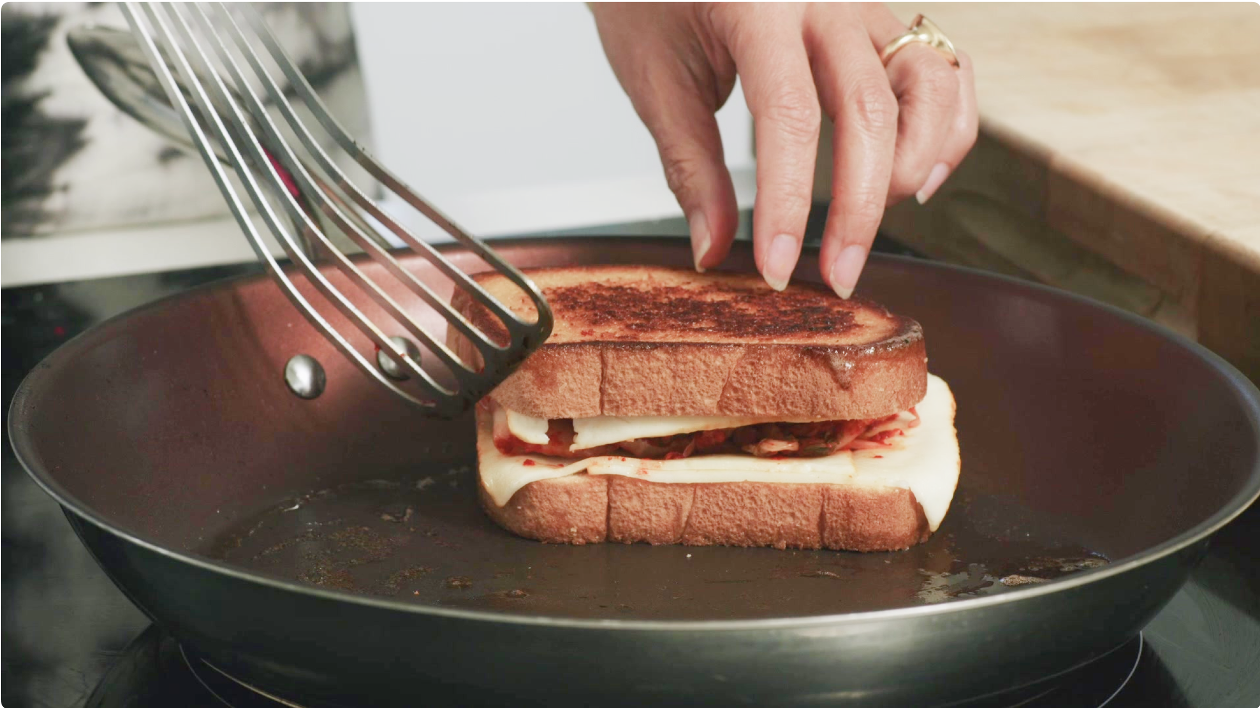 A grilled cheese with kimchi sandwich is cooked in a frying pan.