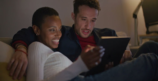 A couple watches media on their tablet while sitting on a couch.