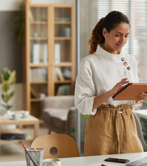 Photo of a businesswoman using a digital tablet while standing by a desk in an office space