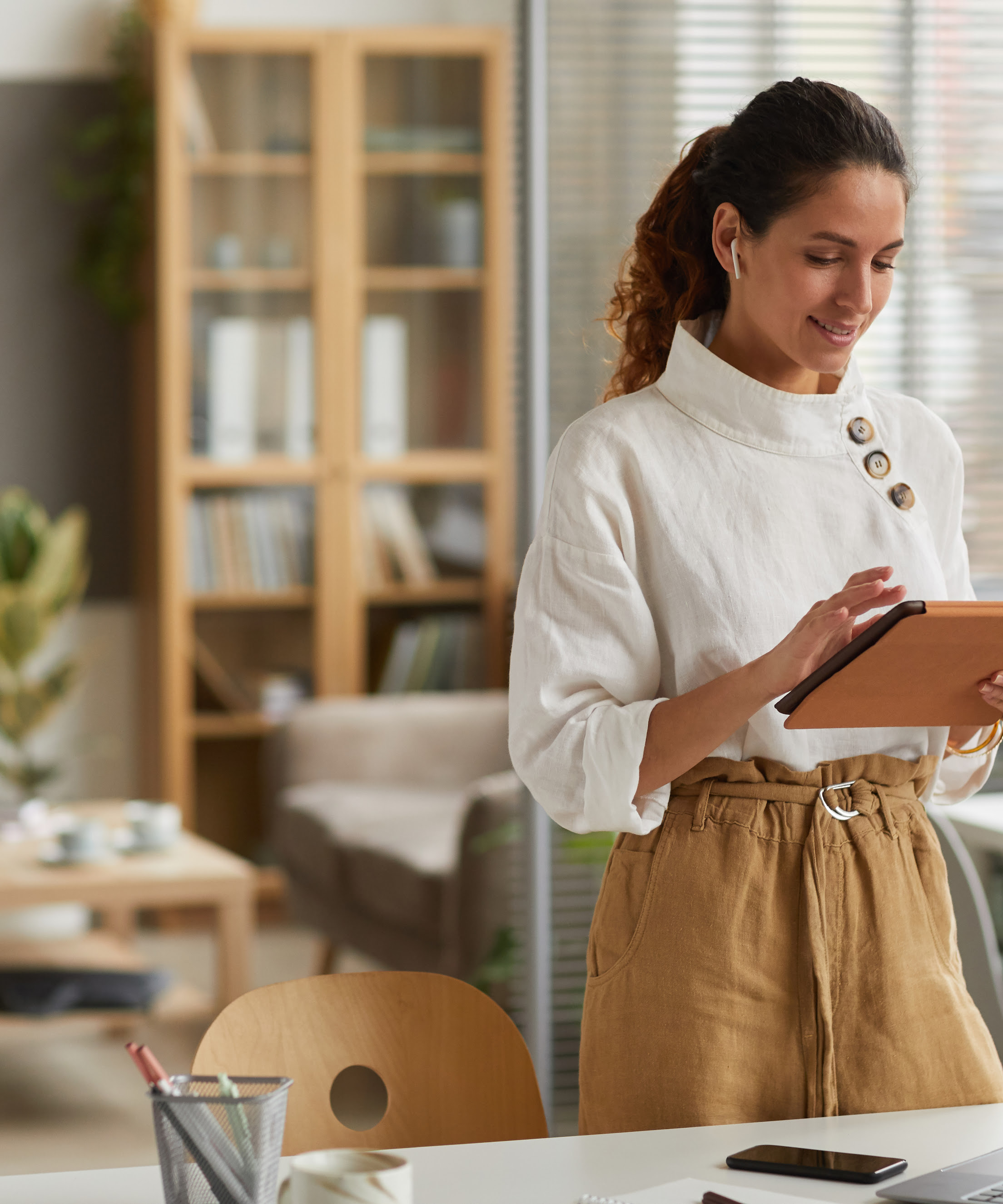 Photo of a businesswoman using a digital tablet while standing by a desk in an office space