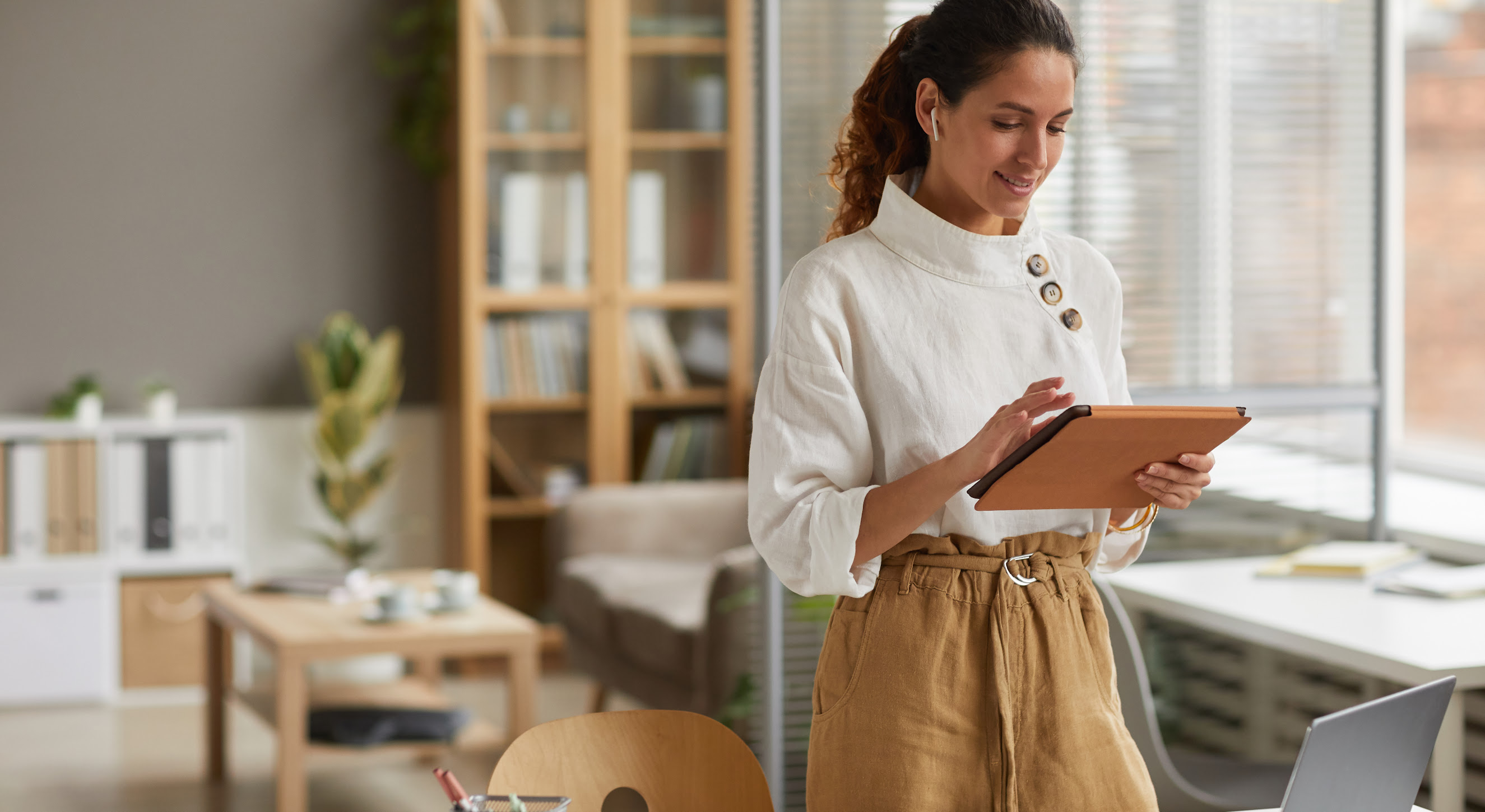 Photo of a businesswoman using a digital tablet while standing by a desk in an office space