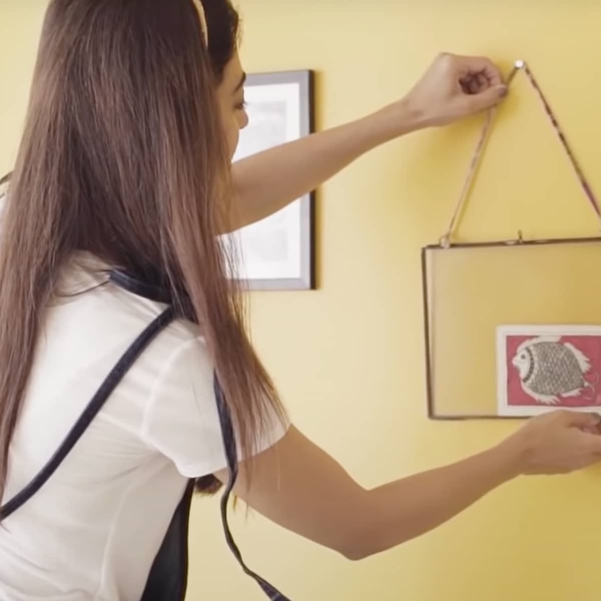 A woman hanging decor on a yellow painted wall