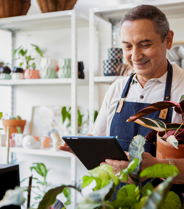 A garden store employee behind a counter with a counter with a tablet in his hand.