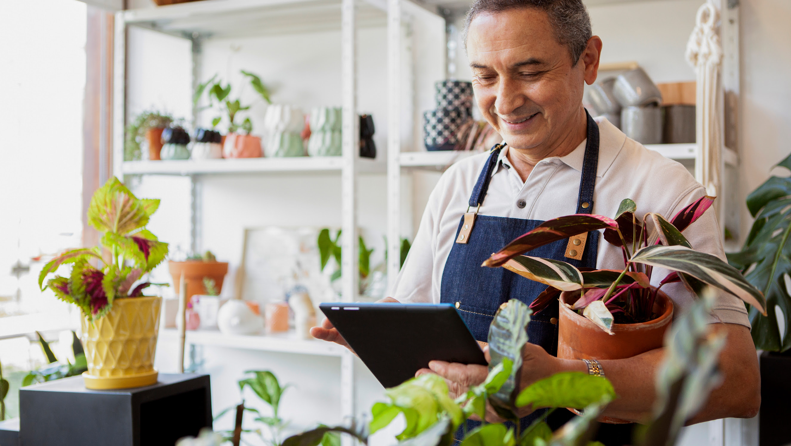 A garden store employee behind a counter with a counter with a tablet in his hand.