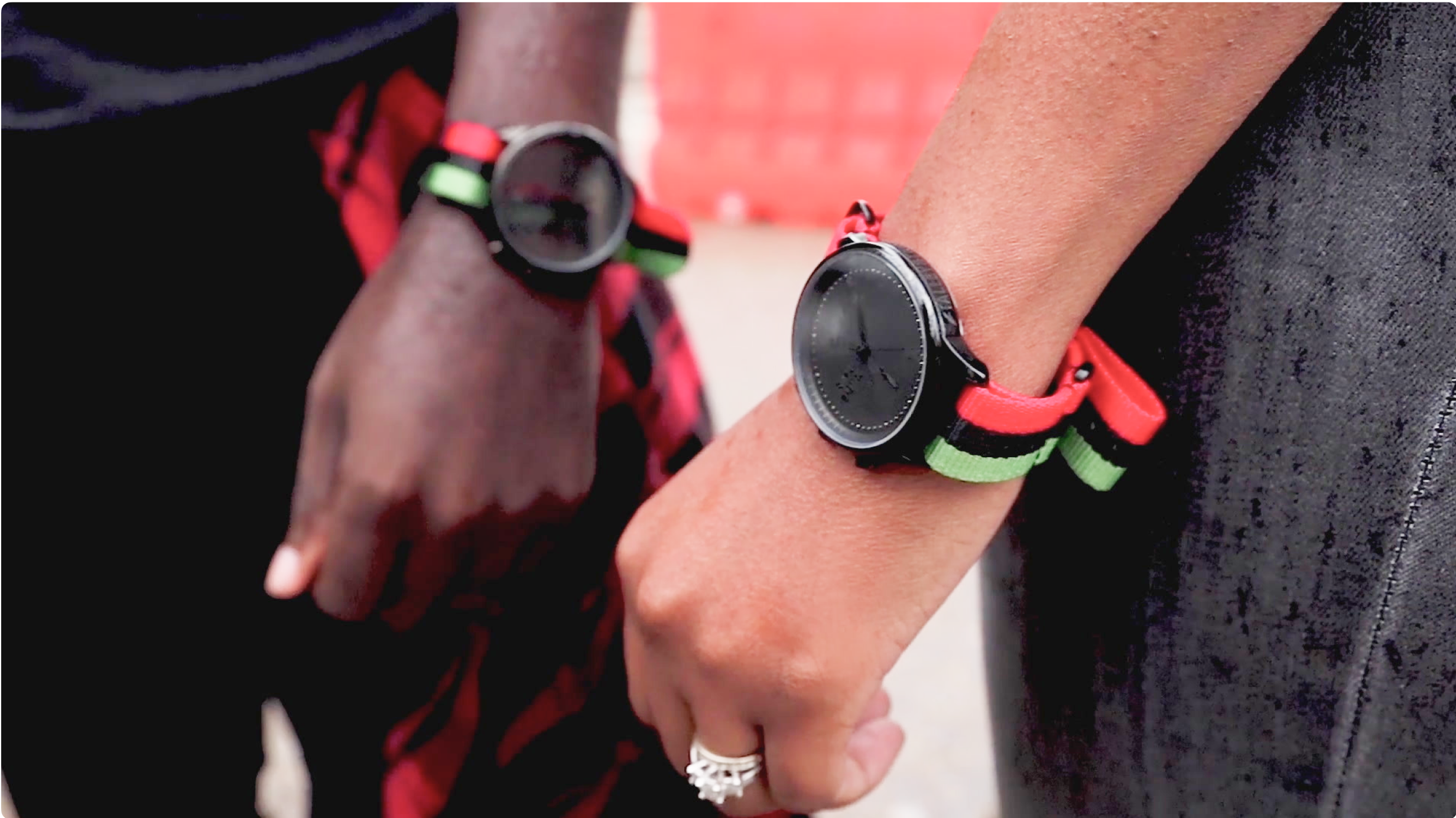 A man and woman wear matching Talley & Twine watches. The watches have black faces and bands striped with red, black, and green.