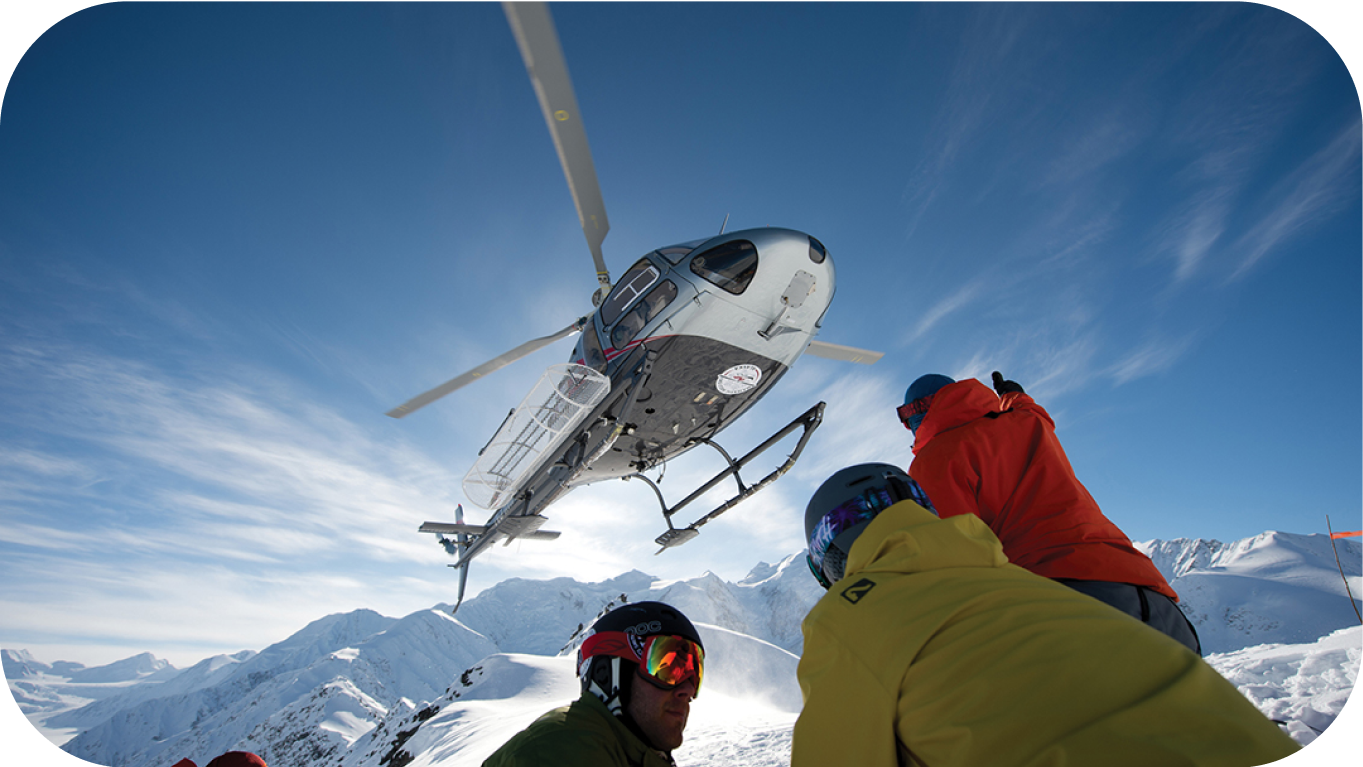 Image of a Heli Ski helicopter above a group of skiers on a mountain top.