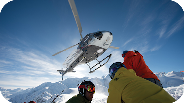 Image of a Heli Ski helicopter above a group of skiers on a mountain top.