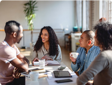 Four people of different genders and ethnicities have a conversation over coffee.