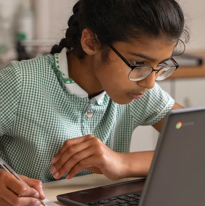 A student takes notes while learning from a laptop