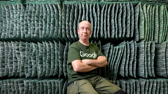 A photograph of a smiling man in a Google branded tshirt in a Google facility. 