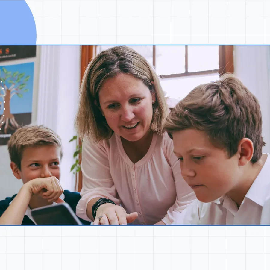 A teacher explains a topic to two seated students in a classroom setting