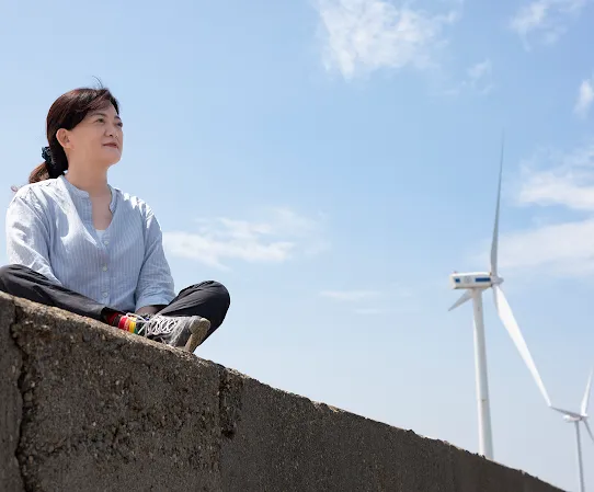 Googler Melody Chang sits on a wall with a windmill in the background in Changhua County Taiwan