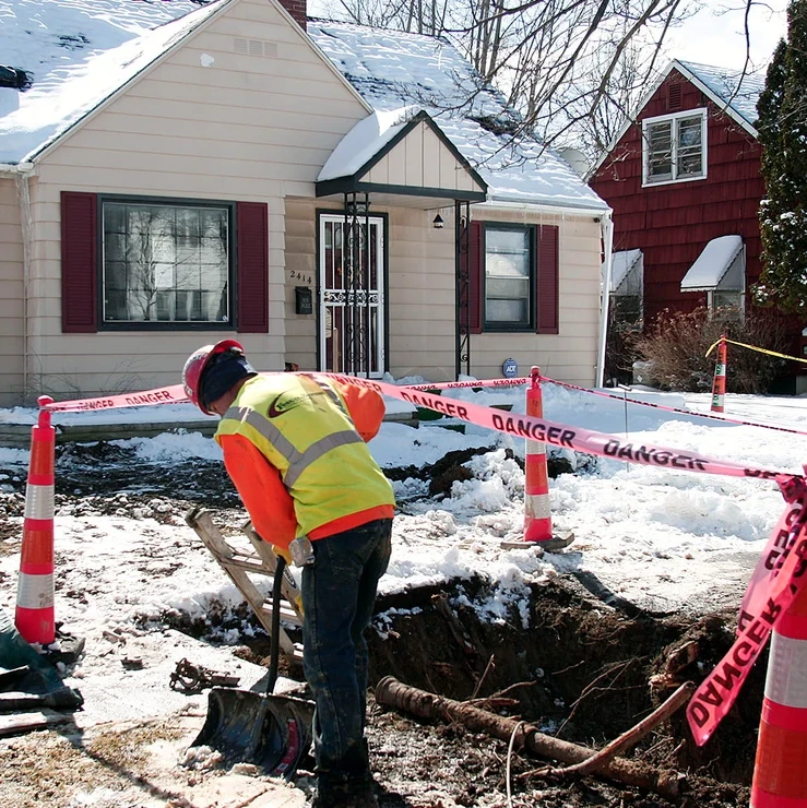 A photograph of a construction worker digging in a residential neighbor during the winter