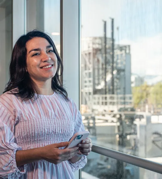 Googler Pia Quiroz smiles with the Quilicura Chile data center in the background outside the windows behind her