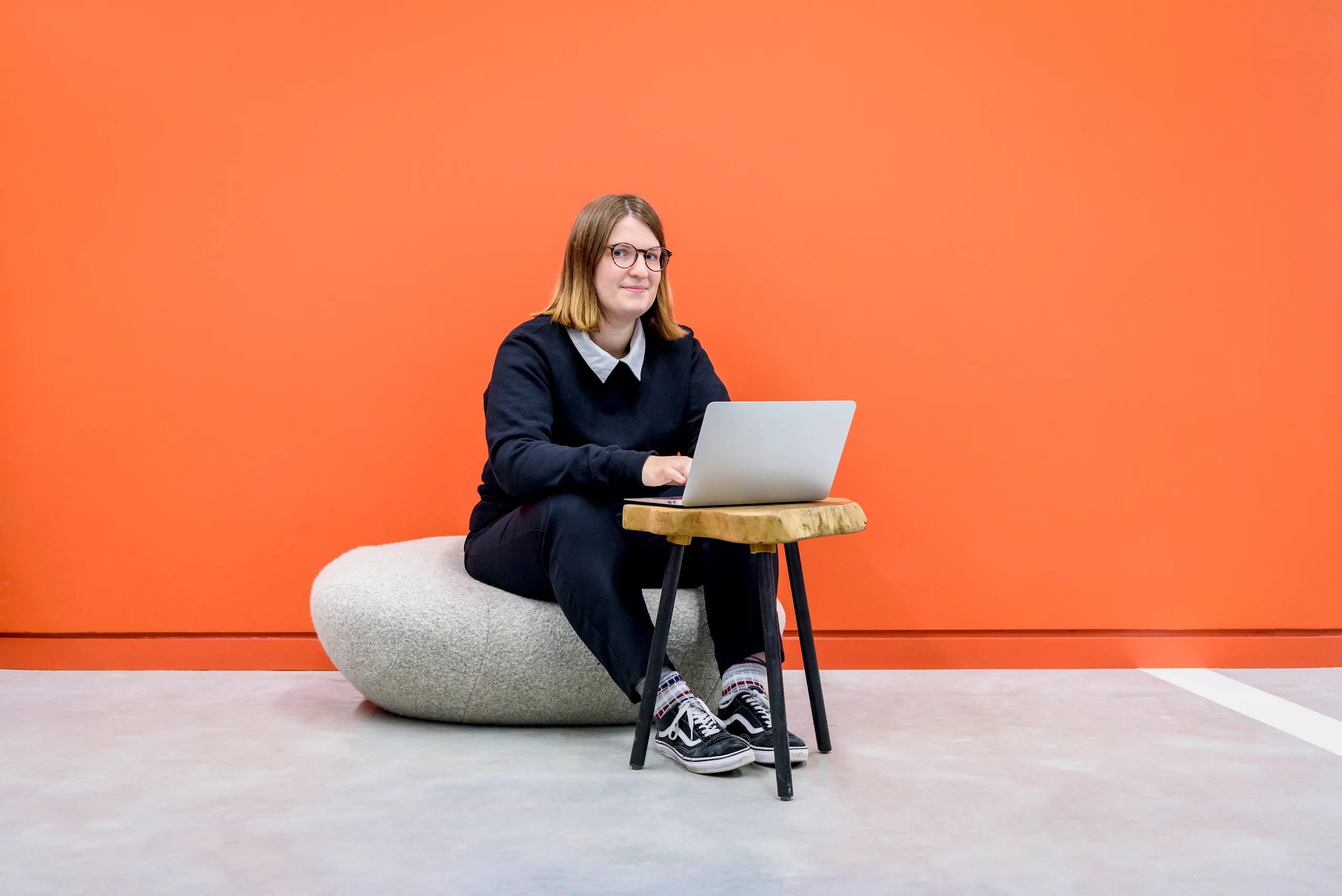 A photograph of a woman sitting down with a laptop looking at the camera.