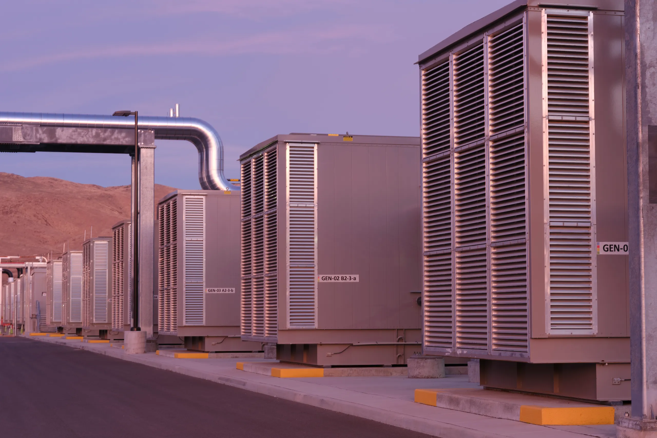 An exterior photograph of backup generators in Storey County, Nevada, data centers at dusk with the Flowery Mountain range in the background.