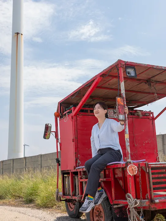 Googler Melody Chang sits on a red vehicle with a windmill in the background in Changhua County Taiwan