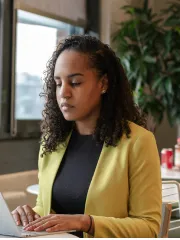 A woman in a yellow blazer works on her laptop