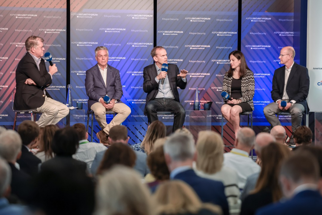 Five people on a stage with microphones in their hand having a panel discussion in front of an audience.