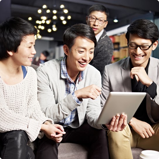 A diverse team huddles around one team member holding an open file and reviewing its contents.