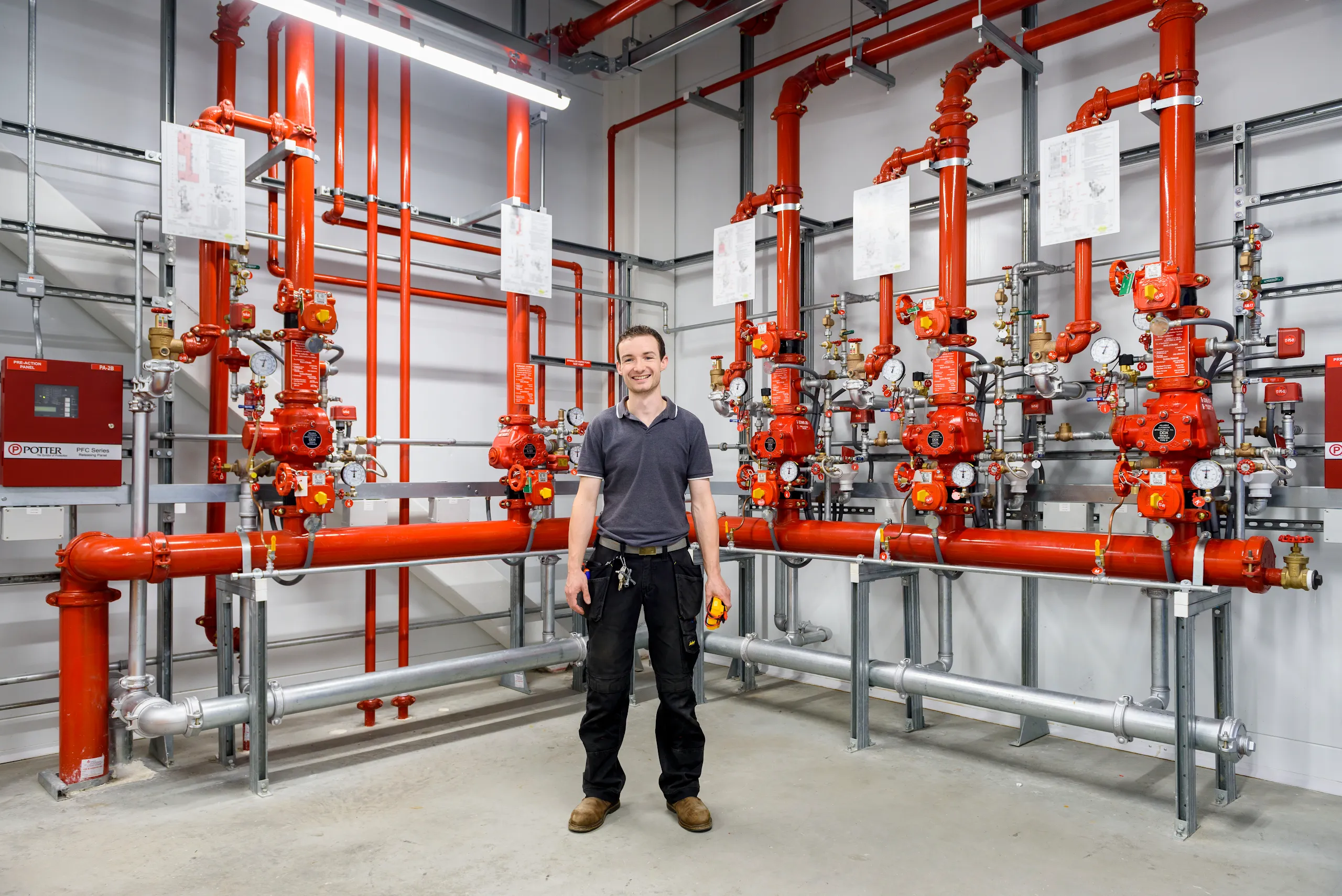 A photograph of a smiling man standing in front of pipes inside a Google facility. 