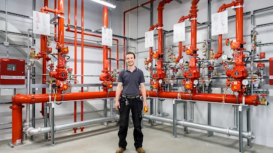 A photograph of a smiling man standing in front of pipes inside a Google facility. 