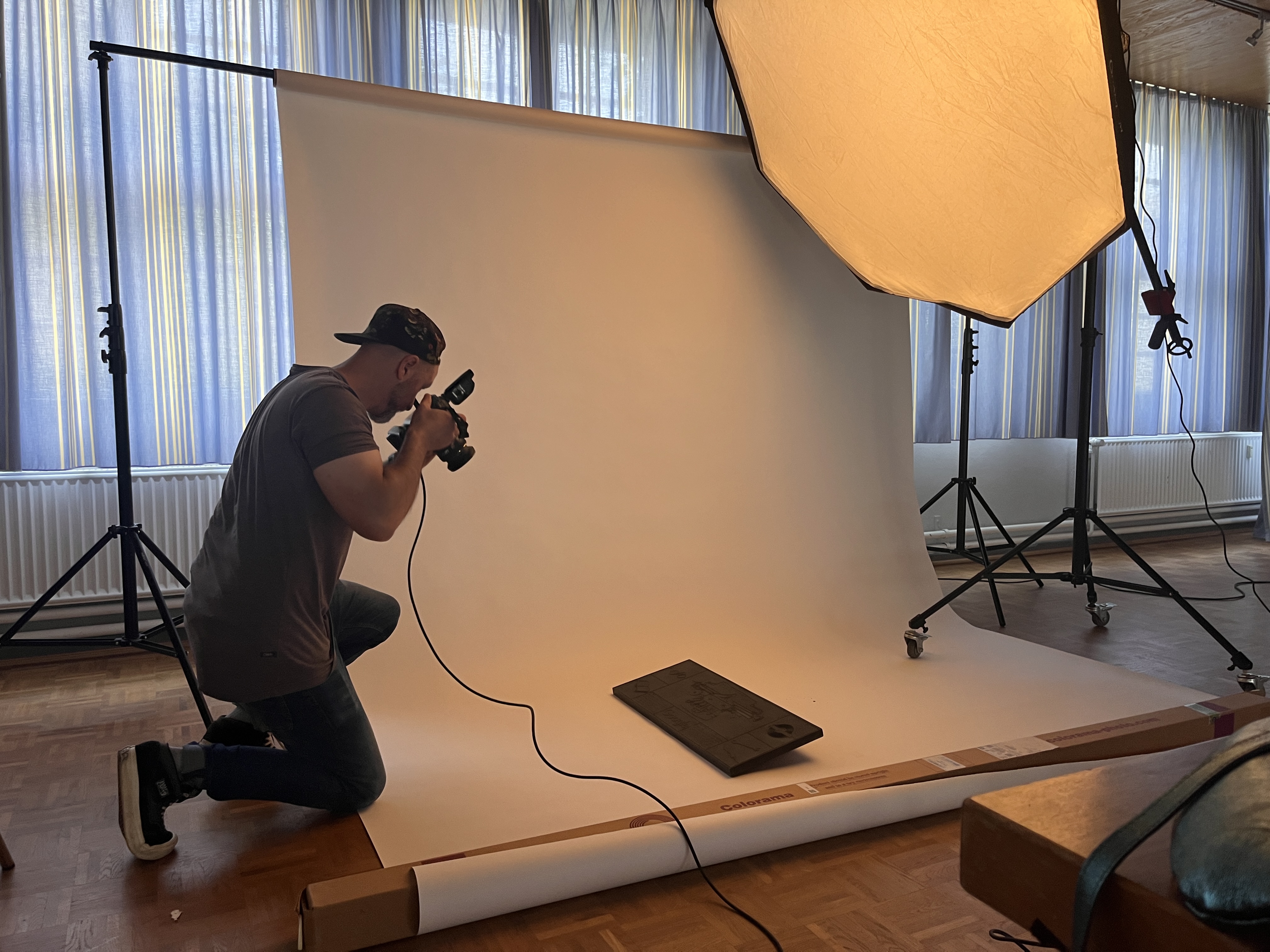 A photograph of a man kneeling in a studio holding a camera pointed towards the Doodle with a big light overhead.