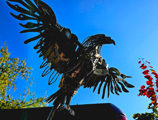 Photo of eagle made from different types of scrap metal material with open wings and bright blue sky.