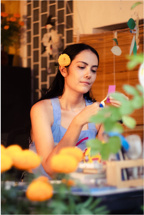 Photograph of Hispanic woman wearing a blue tank to with long black hair and a yellow flower tucked behind her ear