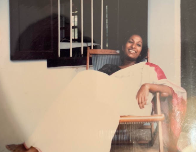 A Photograph of Meena sitting on a chair and smiling.
