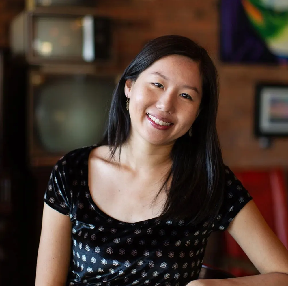 Photograph of a woman with dark hair wearing a black shirt smiling into the camera.