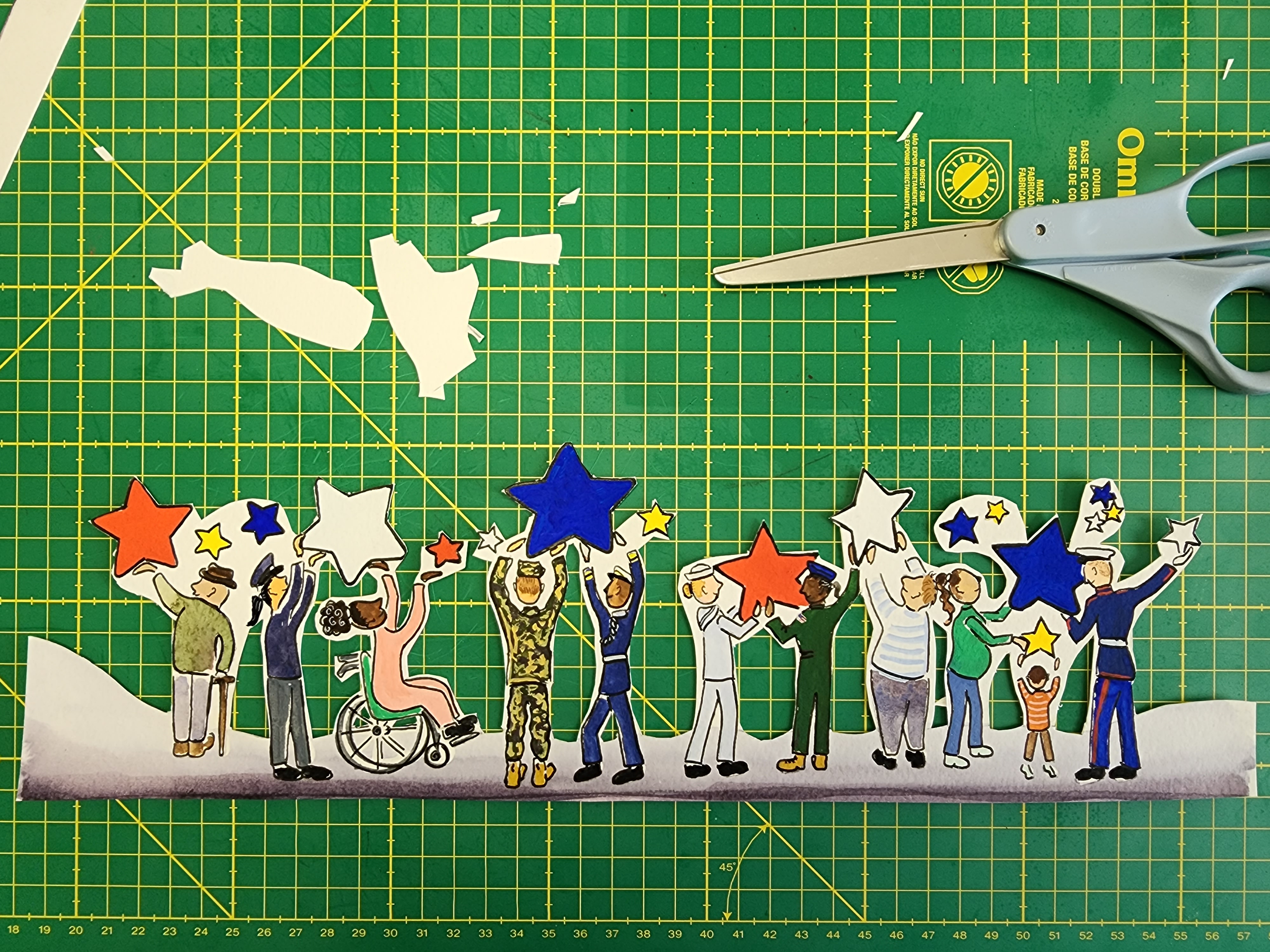 Photo of a paper cut out of people holding stars sitting on a work table with scissors in frame